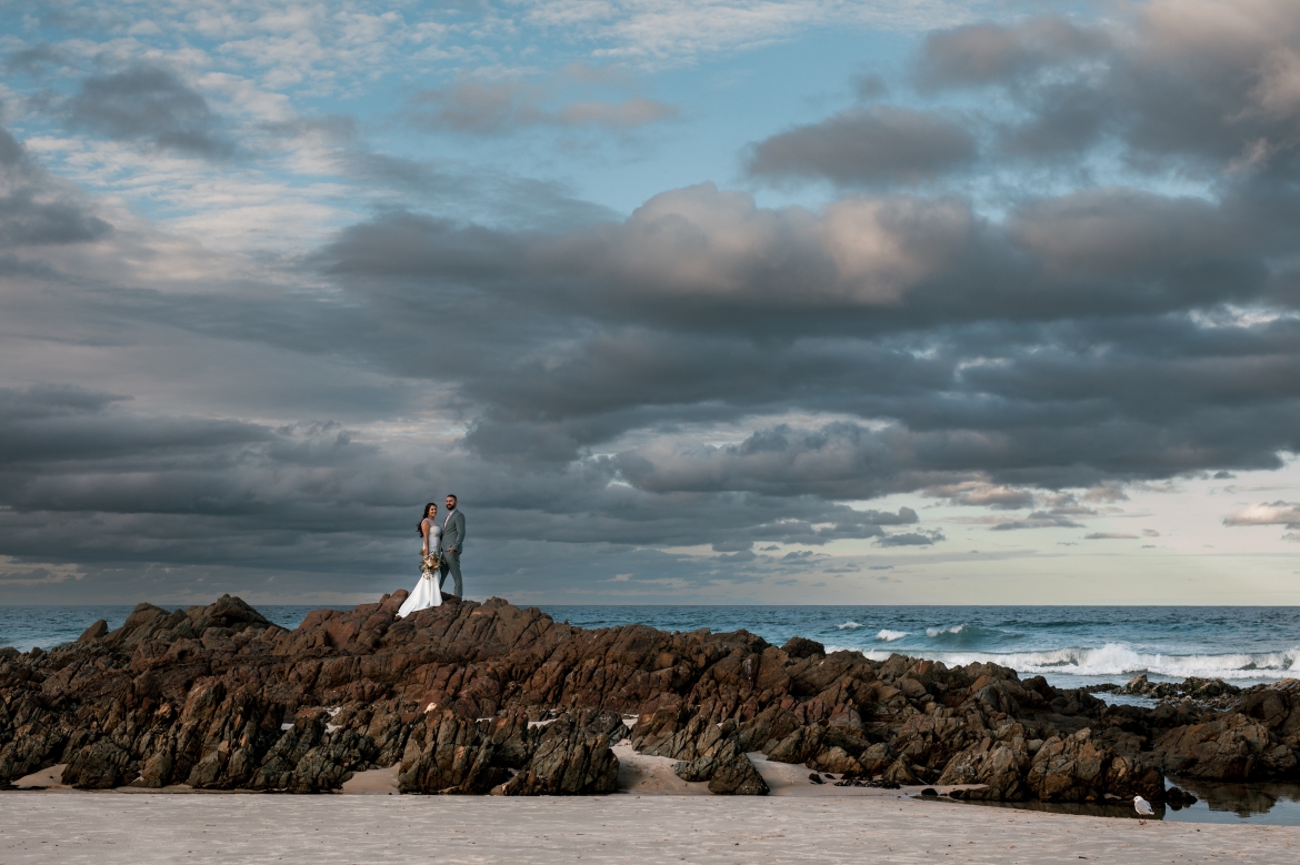 cabrita beach nsw landscape beach photo with elopement couple standing on rocks and stormy skies