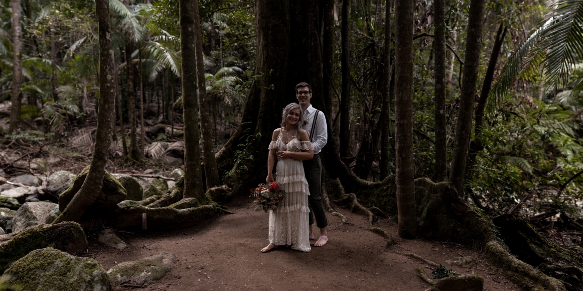 the wedding couple standing beneath the fig tree at Crystal creek rainforest retreat elopement with bohoelope