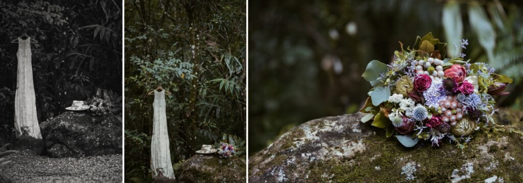 The brides lace wedding dress suspended from a branch with the beautiful bouquet in colours of deep purples and red, with a native earthy base.