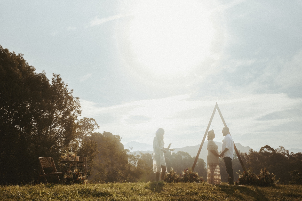 Bride wearing a Jaase dress and groom with their celebrant in front of a triangle arbour late afternoon hill top elopement at Bunyarra in Crystal Creek NSW